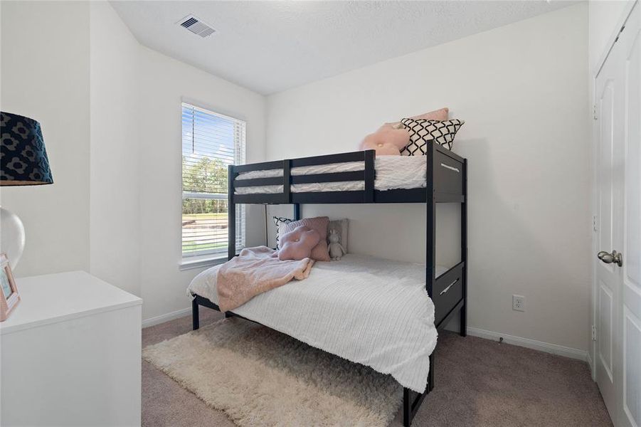 Secondary bedroom features plush carpet, high ceilings, ample closet space, and a large window with privacy blinds.