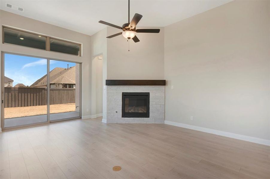 Unfurnished living room with ceiling fan, light wood-type flooring, a high ceiling, and a fireplace Unfurnished living room with ceiling fan, light wood-type flooring, a high ceiling, and a fireplace