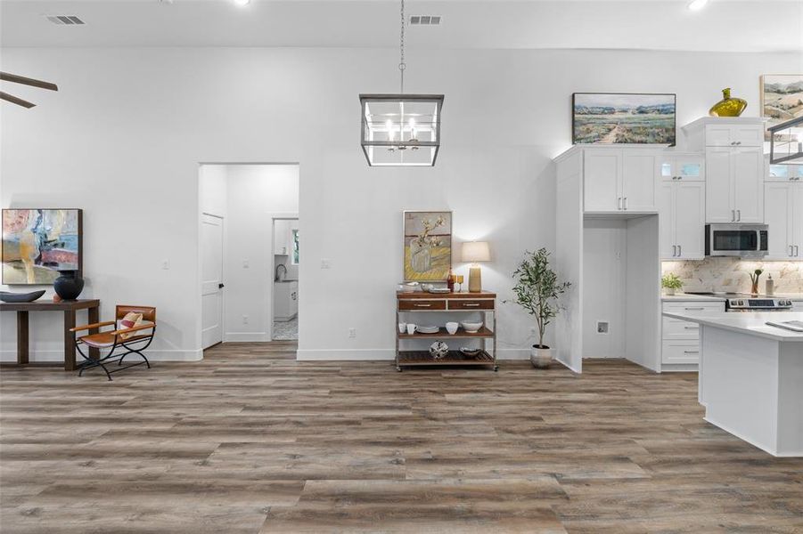 Kitchen featuring ceiling fan with notable chandelier, backsplash, white cabinetry, and hardwood / wood-style flooring