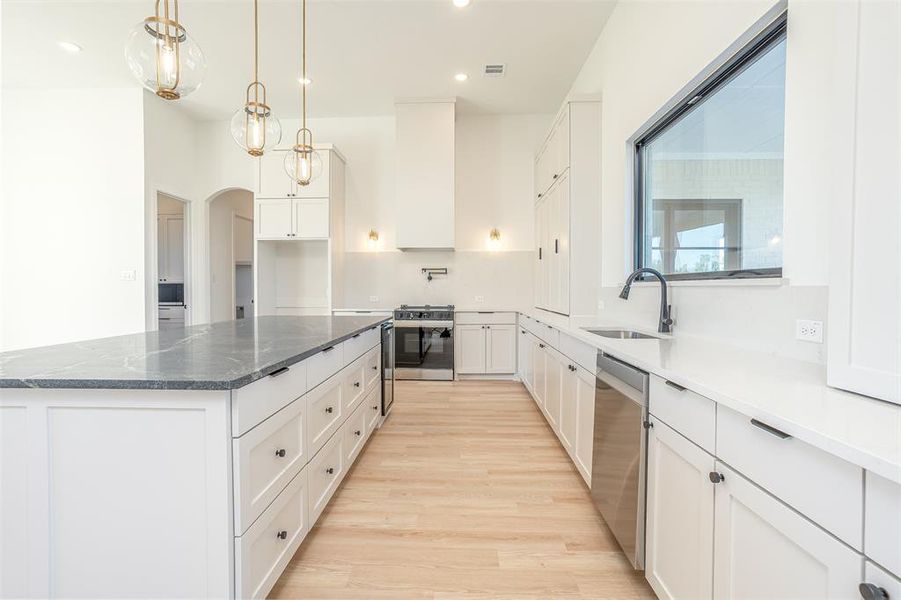 Kitchen featuring sink, stainless steel appliances, white cabinets, a kitchen island, and light wood-type flooring