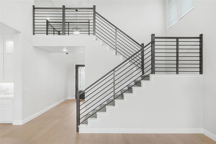 Open two-story staircase with dark metal railing, white walls, and light hardwood floors