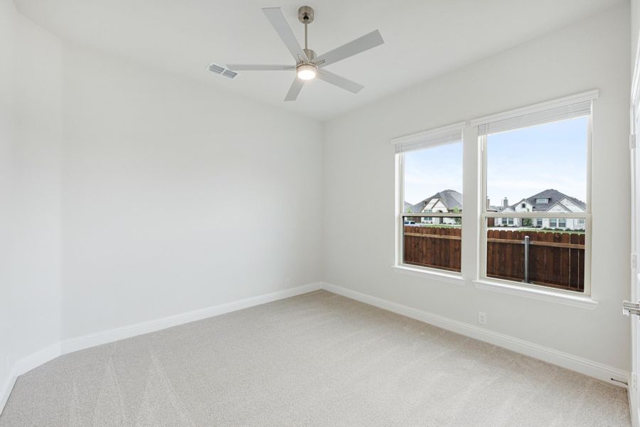 Empty bedroom with carpet flooring, ceiling fan, and double windows overlooking a wood fence and neighboring homes Empty bedroom with carpet flooring, ceiling fan, and double windows overlooking a wood fence and neighboring homes