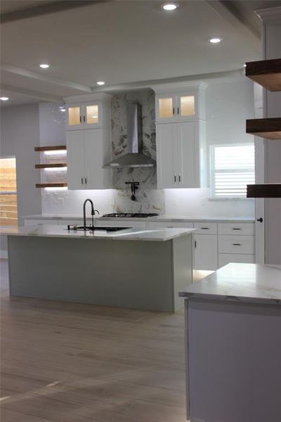 Kitchen featuring wall chimney range hood, sink, light wood-type flooring, a center island, and white cabinets