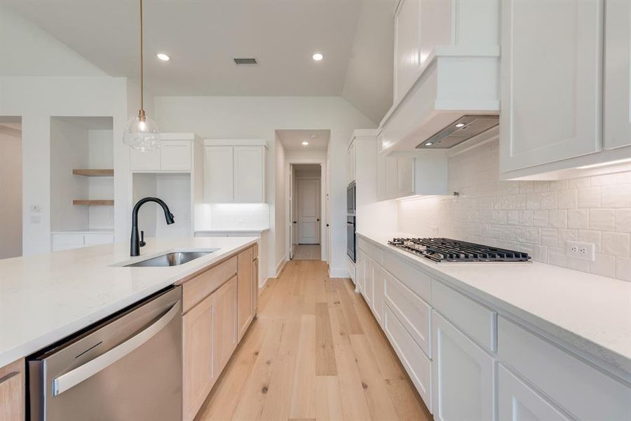 Kitchen featuring decorative light fixtures, appliances with stainless steel finishes, light wood-style floors, light stone counters, and recessed lighting