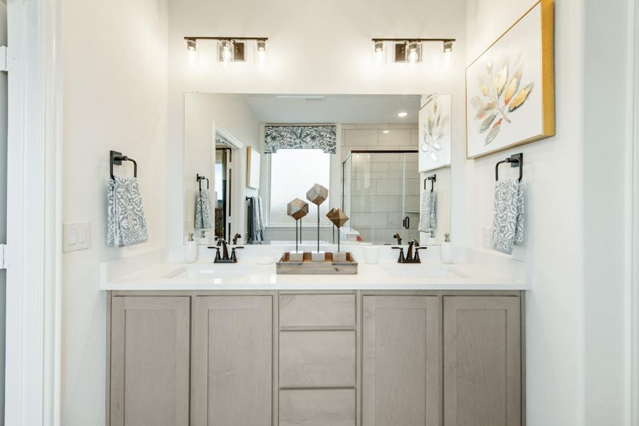 Bathroom double vanity with gray cabinets, white countertop, two sinks, and large mirror with overhead lighting Bathroom double vanity with gray cabinets, white countertop, two sinks, and large mirror with overhead lighting