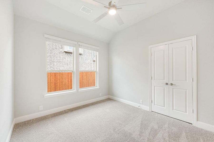 Empty bedroom with carpet flooring, ceiling fan, double closet doors, and a window with backyard view