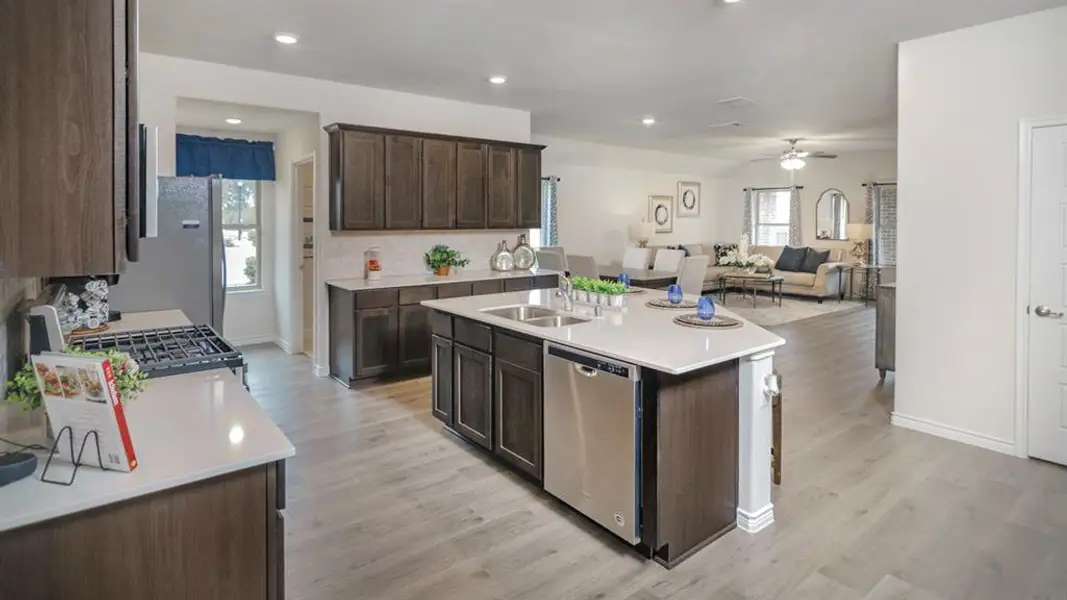 Contemporary kitchen featuring wood-finish cabinetry, light-toned countertops, stainless steel appliances, and a central island with an integrated sink