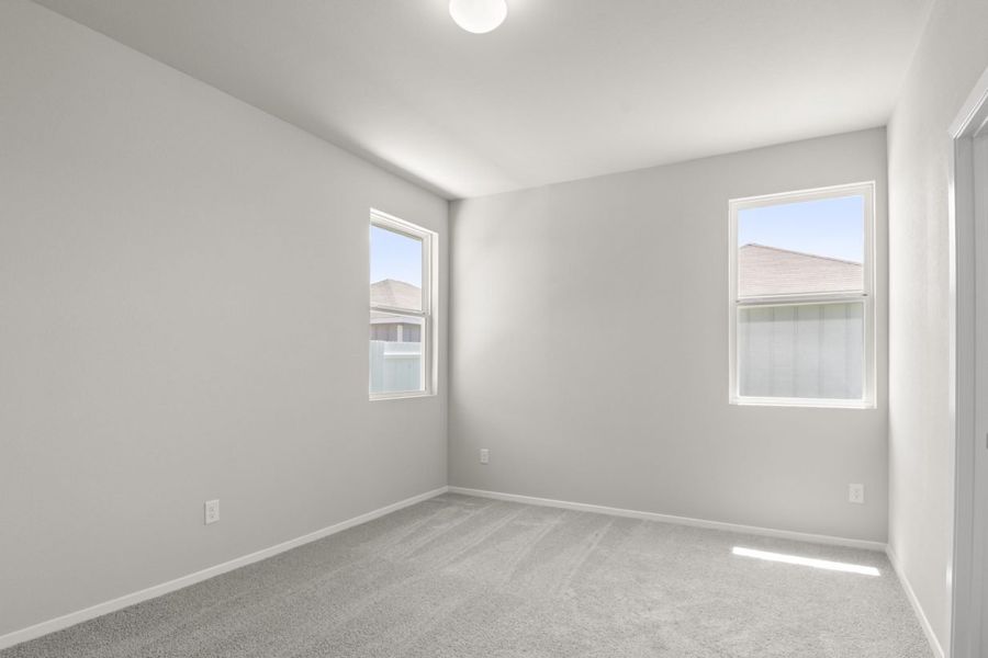 A bedroom with cream colored walls, white framed windows, and tan carpeting.