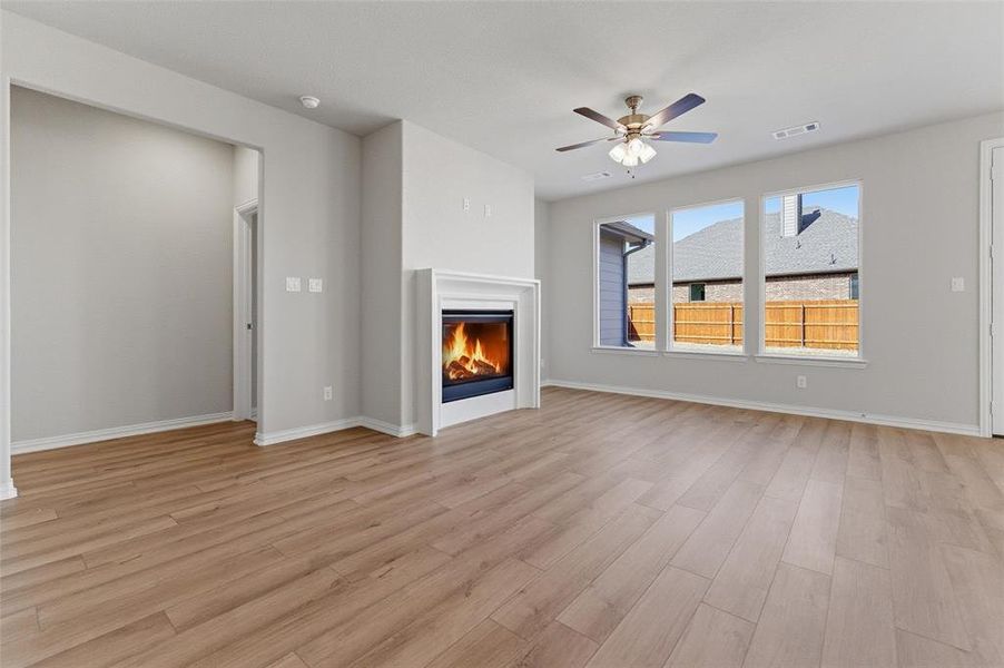 Unfurnished living room featuring a glass covered fireplace, ceiling fan, and light wood-style flooring