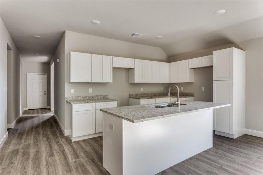 Kitchen featuring white cabinets, light stone counters, light wood finished floors, and vaulted ceiling