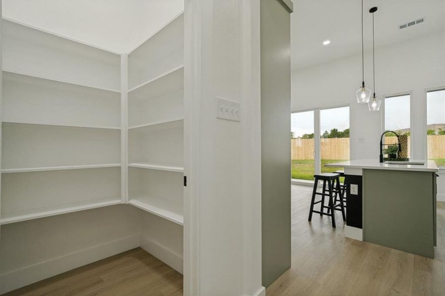 Walk-in pantry featuring extensive built-in shelving, wood-finish flooring, and bright white walls Walk-in pantry featuring extensive built-in shelving, wood-finish flooring, and bright white walls