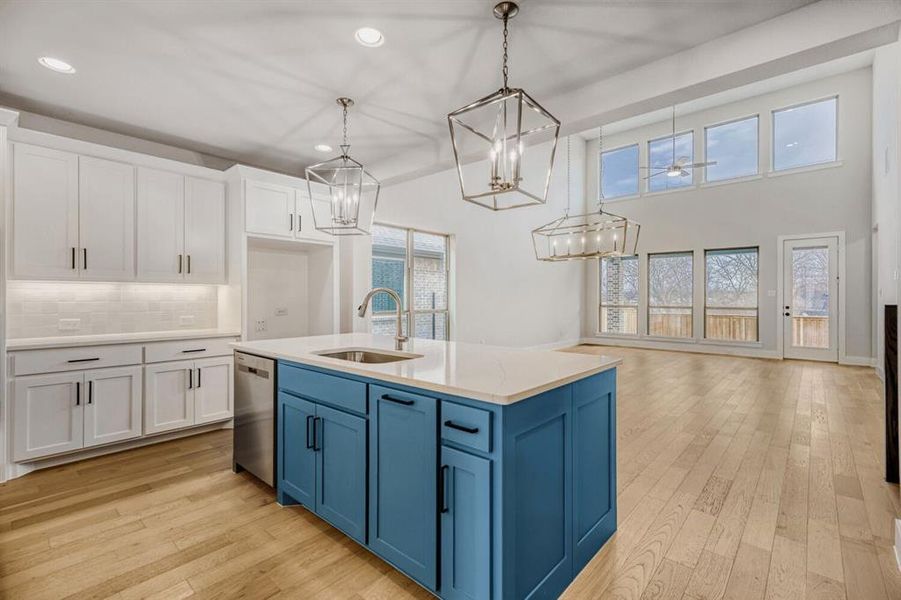 Dual tone kitchen featuring two tone cabinets, light wood-type flooring, a kitchen island with sink, light stone counters, and decorative backsplash