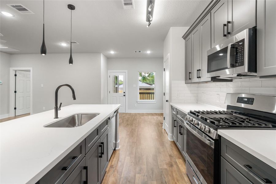 This modern kitchen features sleek gray cabinetry, stainless steel appliances, and a spacious island with a sink. The room is bright with recessed lighting and pendant lamps, and it has a stylish wood floor. This modern kitchen features sleek gray cabinetry, stainless steel appliances, and a spacious island with a sink. The room is bright with recessed lighting and pendant lamps, and it has a stylish wood floor.