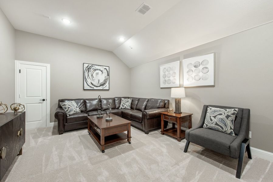Living room with dark leather sectional sofa, gray accent chair, and vaulted ceiling over light carpet Living room with dark leather sectional sofa, gray accent chair, and vaulted ceiling over light carpet