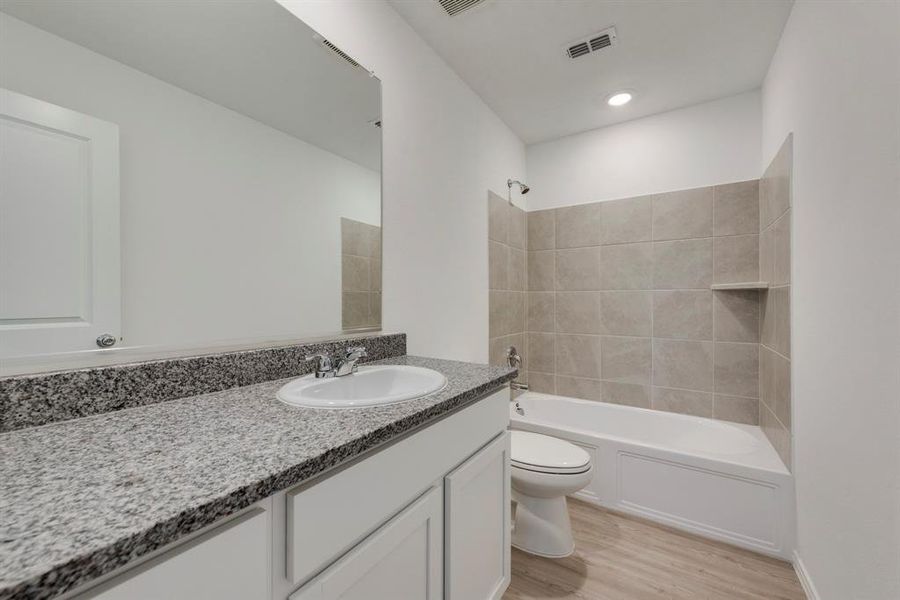 Full bathroom featuring hardwood / wood-style floors, tiled shower / bath combo, toilet, and vanity