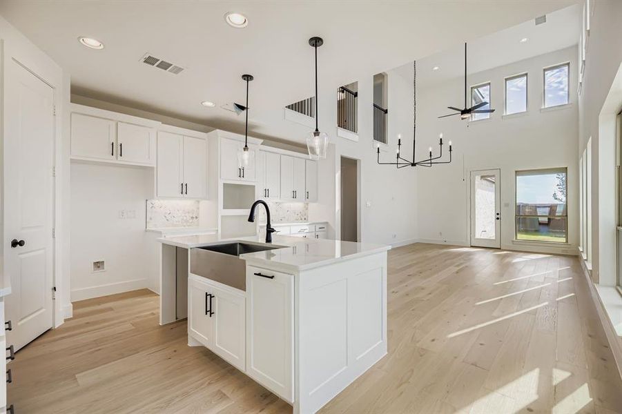 Kitchen featuring decorative light fixtures, white cabinetry, light wood-style floors, decorative backsplash, and a high ceiling Kitchen featuring decorative light fixtures, white cabinetry, light wood-style floors, decorative backsplash, and a high ceiling