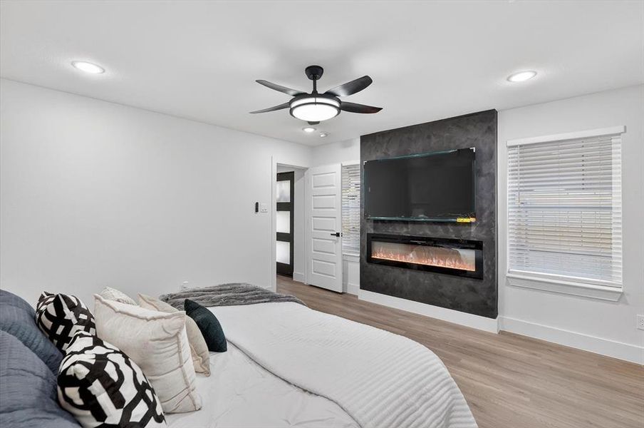 Bright interior featuring wood-finish flooring, a contemporary ceiling fan, recessed lighting, and a dark accent wall with an integrated electric fireplace