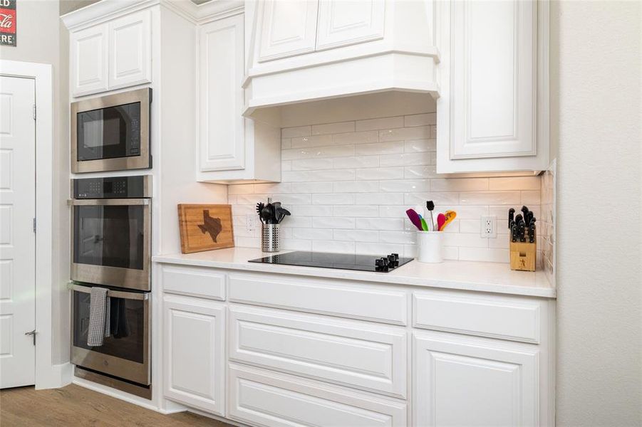 Kitchen with white cabinetry, tasteful backsplash, stainless steel double oven, built in microwave, and light wood-style flooring