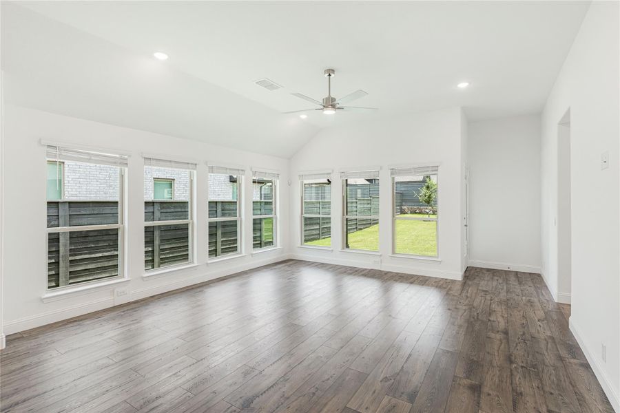 Empty living room with vaulted ceiling, ceiling fan, hardwood floors, and large windows overlooking backyard Empty living room with vaulted ceiling, ceiling fan, hardwood floors, and large windows overlooking backyard