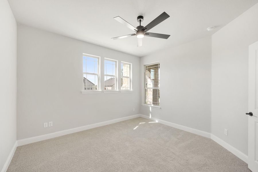 Empty bedroom with carpet flooring, ceiling fan, and three windows with natural light