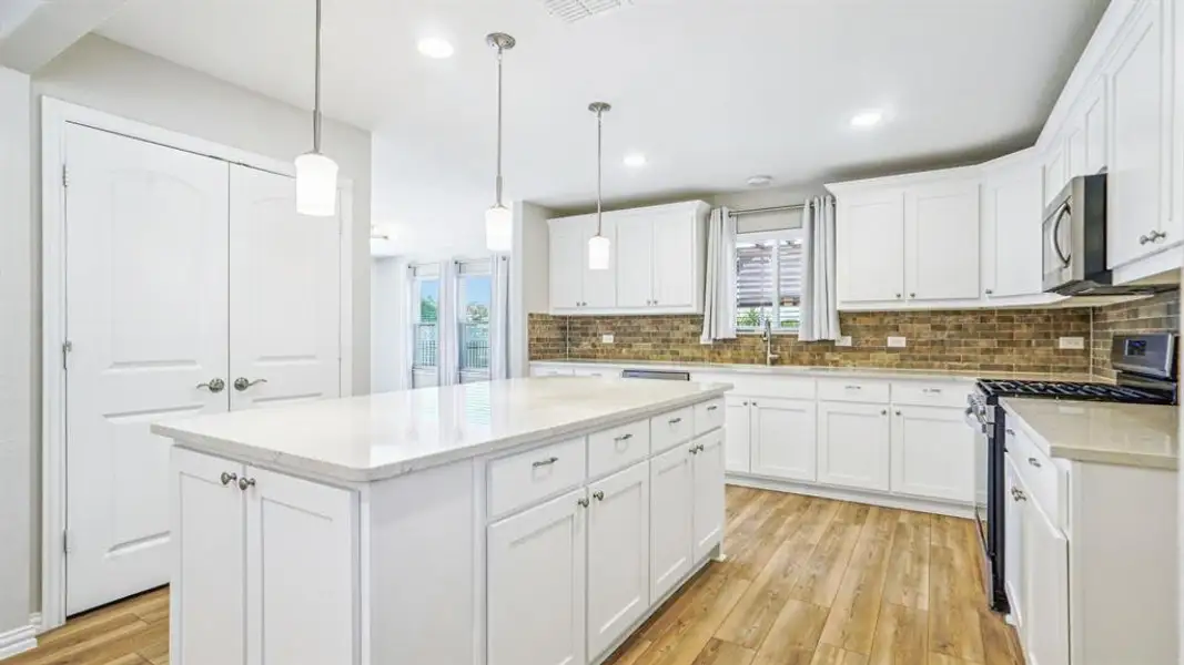 Kitchen with tasteful backsplash, appliances with stainless steel finishes, white cabinetry, light wood-style floors, and pendant lighting Kitchen with tasteful backsplash, appliances with stainless steel finishes, white cabinetry, light wood-style floors, and pendant lighting