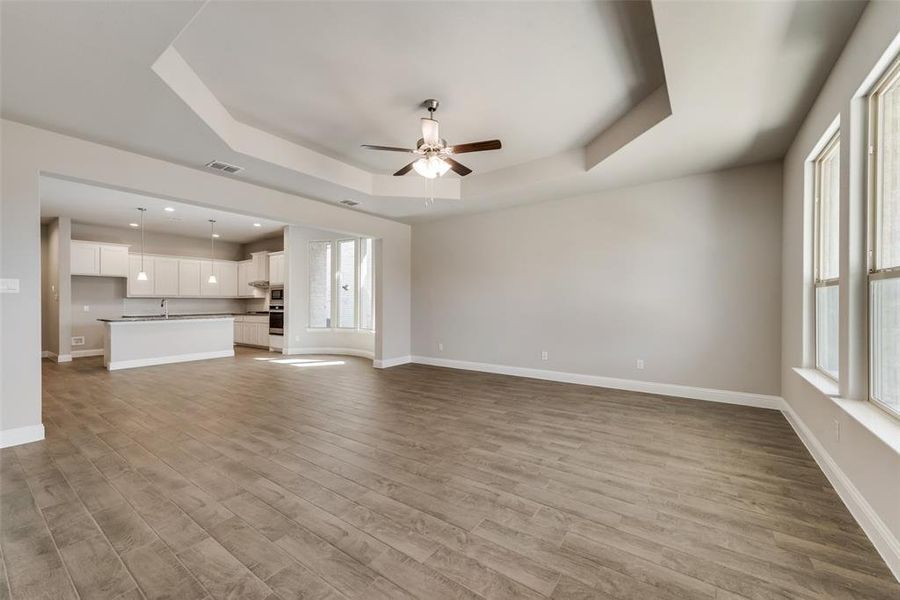 Unfurnished living room with ceiling fan, a tray ceiling, light hardwood / wood-style floors, and a wealth of natural light