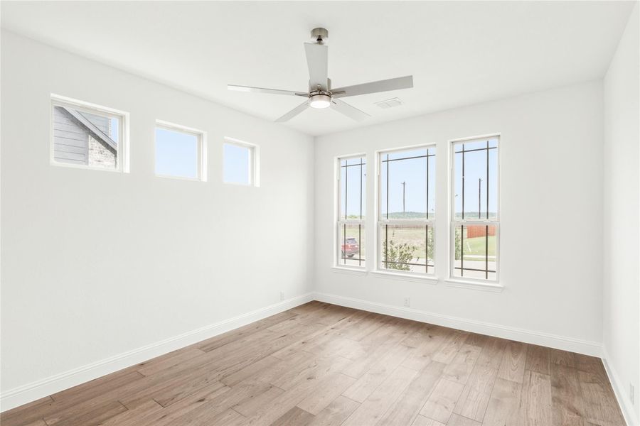 Empty room with light wood floors, ceiling fan, and multiple windows with outdoor views