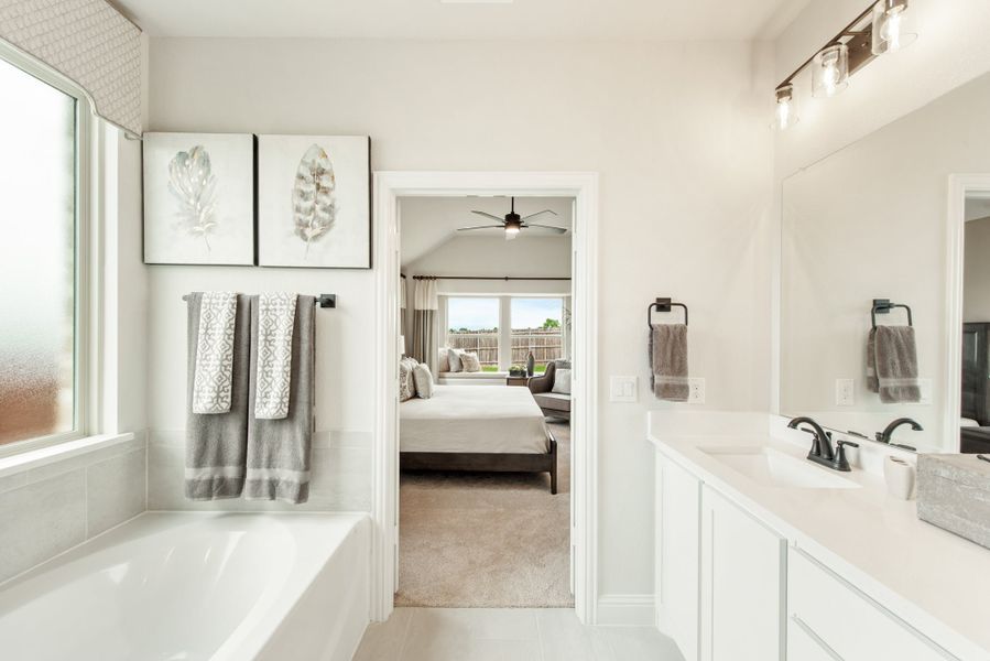 Ensuite bathroom with soaking tub, white vanity, and open view into master bedroom with vaulted ceiling