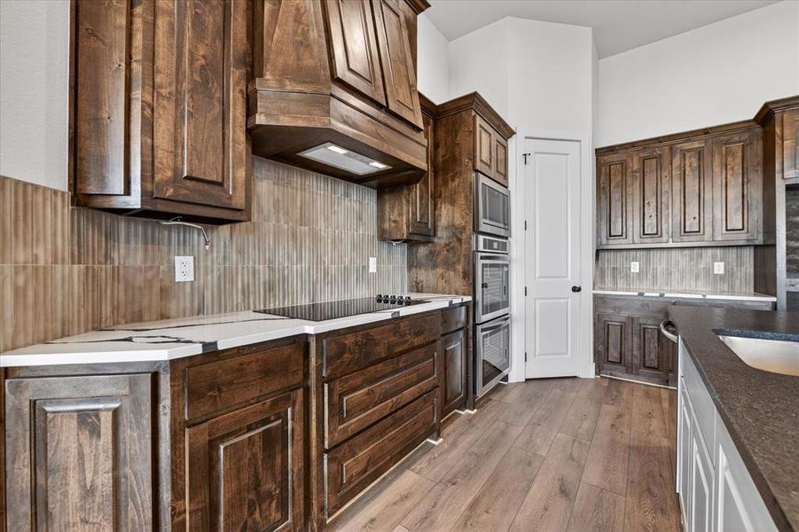 Kitchen with backsplash, light wood-style floors, dark wood finish cabinetry, and stainless steel appliances