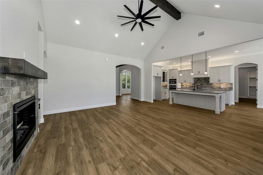Unfurnished living room with ceiling fan, arched walkways, dark wood-type flooring, a fireplace, and beam ceiling