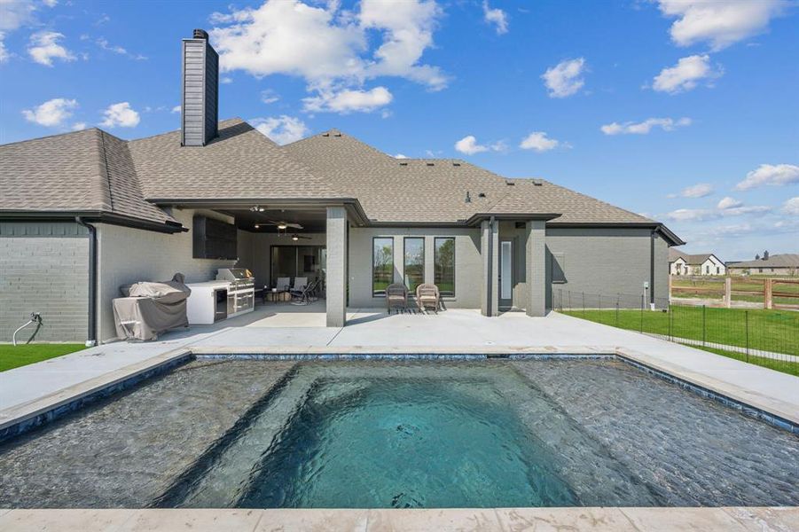 Back of house featuring a shingled roof, a patio, brick siding, a chimney, and area for grilling