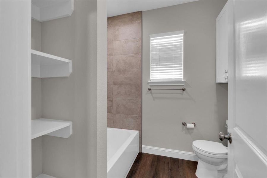 Bathroom with hardwood / wood-style flooring, tiled shower / bath combo, and toilet