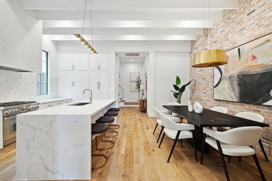 The kitchen and dining room seamlessly flow into the entryway, showcasing 7" European Engineered White Oak Flooring, a charming brick accent wall, and custom beamed ceiling details, creating a warm and inviting atmosphere throughout the space.