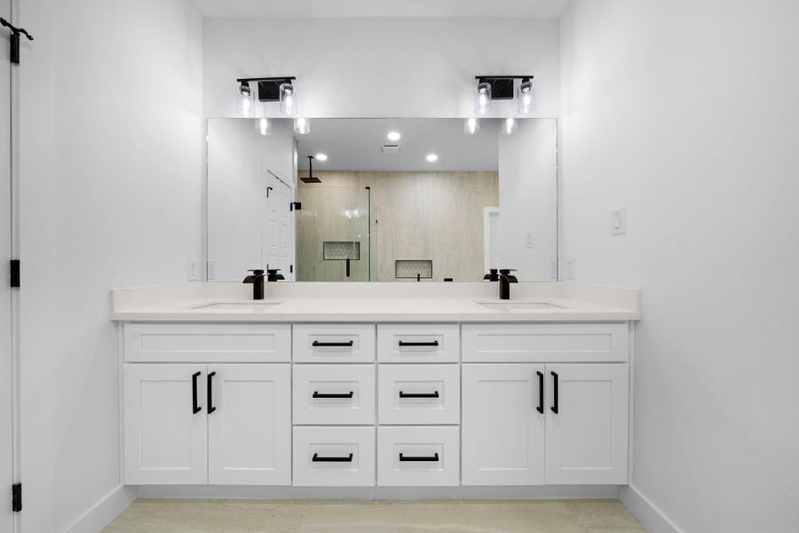 This is primary modern bathroom featuring a double vanity with sleek black fixtures and ample storage in white cabinets. A large mirror and contemporary lighting enhance the space, complementing the neutral tones and clean design. This is primary modern bathroom featuring a double vanity with sleek black fixtures and ample storage in white cabinets. A large mirror and contemporary lighting enhance the space, complementing the neutral tones and clean design.