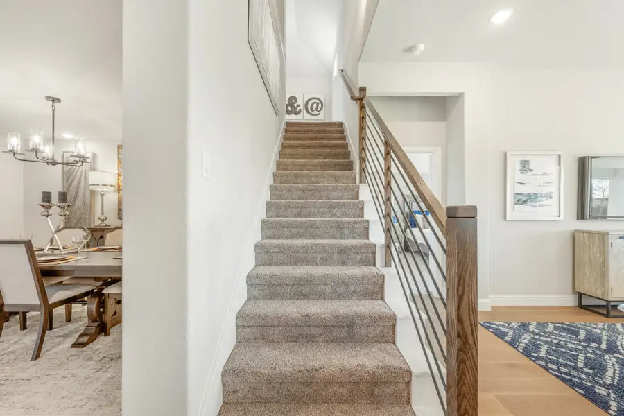 Carpeted staircase with wood and metal railing, dining room visible to the left with chandelier