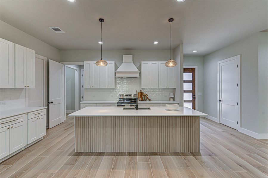 Kitchen with premium range hood, quartz countertops, additional eating at island with basin sink.