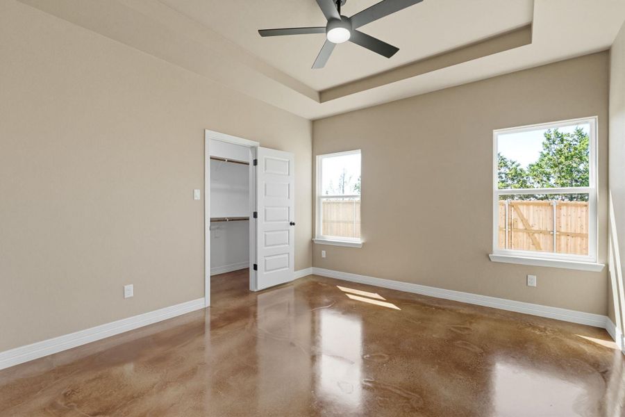 Unfurnished bedroom with concrete floors, a spacious closet, a ceiling fan, and a raised ceiling