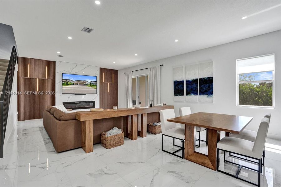 Open-concept living area featuring large format marble-look tile flooring, a built-in electric fireplace, and a wood-slat accent wall with integrated lighting
