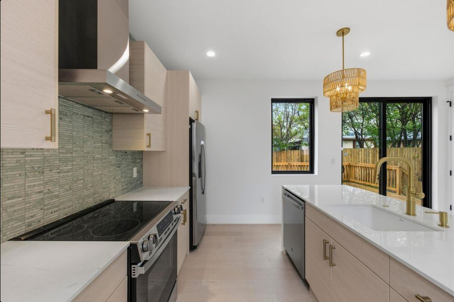Kitchen with light brown cabinetry, stainless steel appliances, wall chimney range hood, modern cabinets, and recessed lighting Kitchen with light brown cabinetry, stainless steel appliances, wall chimney range hood, modern cabinets, and recessed lighting
