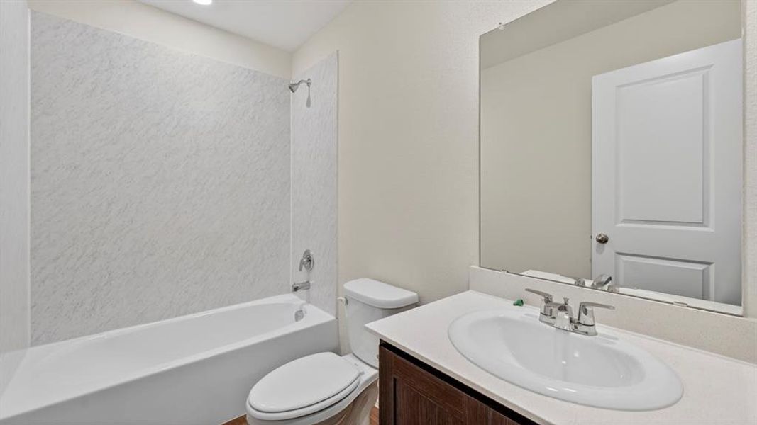Full bathroom featuring a white tub with a textured shower surround, a toilet, and a vanity with an integrated sink and a large mirror