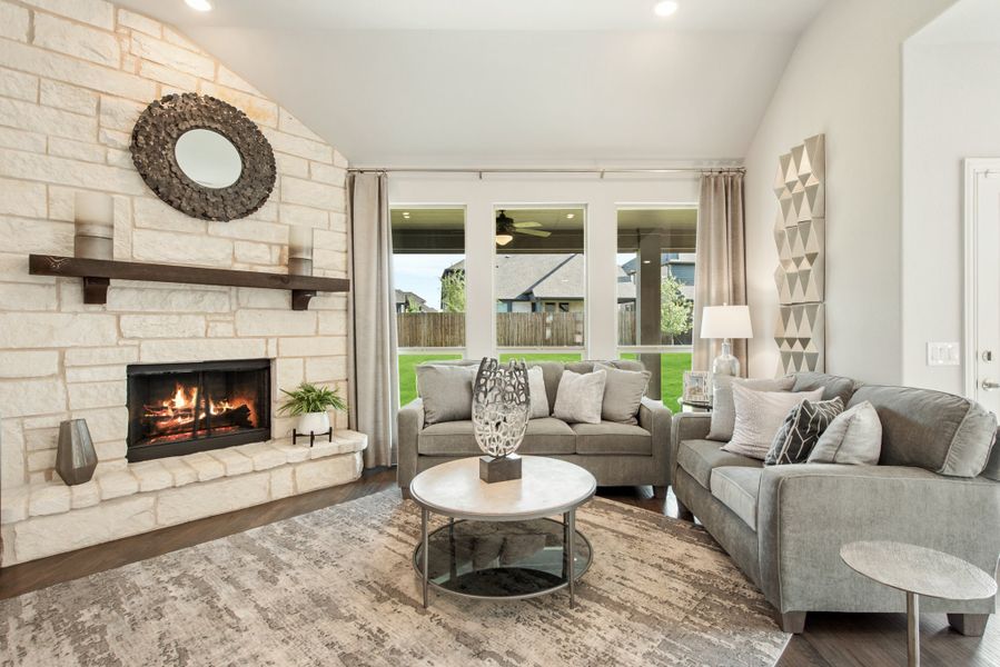 Living room with floor-to-ceiling stone fireplace, gray sofas, and large windows overlooking a backyard patio.