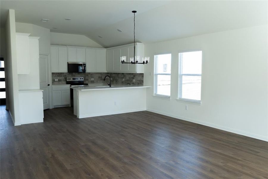 Kitchen featuring vaulted ceiling, a chandelier, open floor plan, light countertops, and white cabinetry