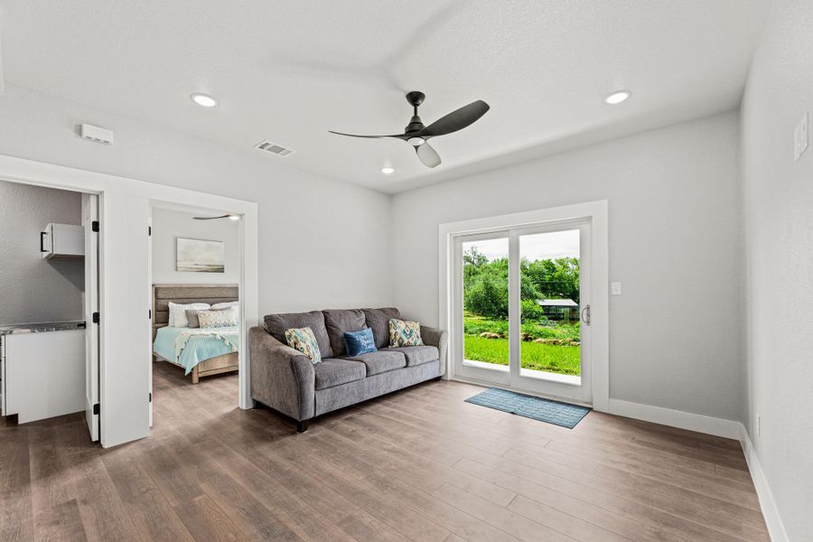 Spacious room featuring wood-finish flooring, a modern ceiling fan, recessed lighting, and a sliding glass door opening to a lush green outdoor area