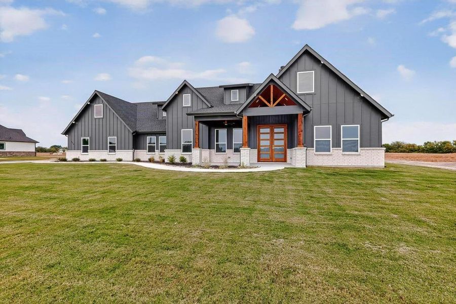 Modern farmhouse style home featuring board and batten siding, a porch, brick siding, french doors, and a front lawn