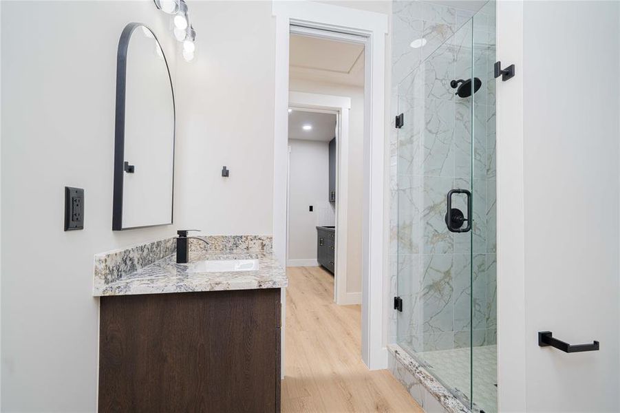 Full bathroom featuring vanity, a marble finish shower, and wood finished floors Full bathroom featuring vanity, a marble finish shower, and wood finished floors