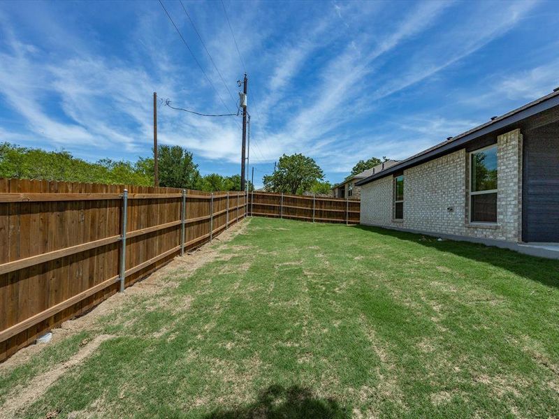 Expansive backyard featuring a new wood privacy fence, freshly laid sod, and a light brick exterior with dark trim Expansive backyard featuring a new wood privacy fence, freshly laid sod, and a light brick exterior with dark trim