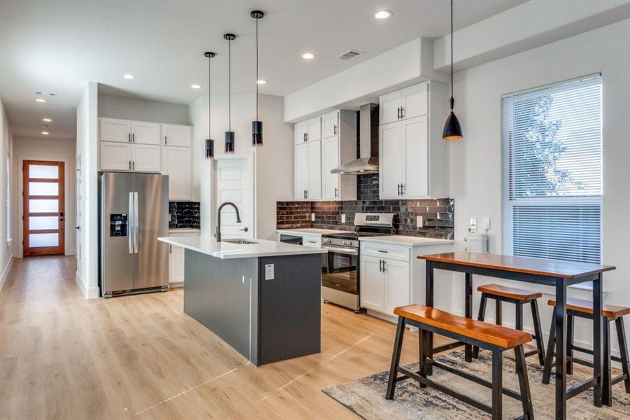 Kitchen featuring pendant lighting, wall chimney exhaust hood, white cabinets, and appliances with stainless steel finishes