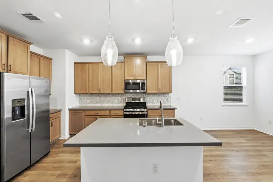 Kitchen with stainless steel appliances, a center island with sink, light wood-style flooring, backsplash, and decorative light fixtures