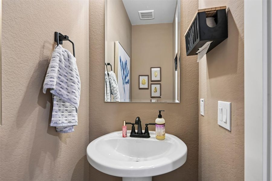 Small powder room with white pedestal sink, black faucet, wall mirror, and towel bar on beige textured walls Small powder room with white pedestal sink, black faucet, wall mirror, and towel bar on beige textured walls