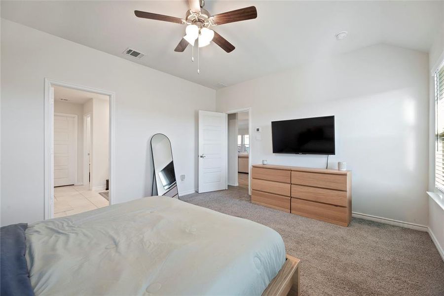 Bedroom with light carpet, multiple windows, a ceiling fan, vaulted ceiling, and connected bathroom